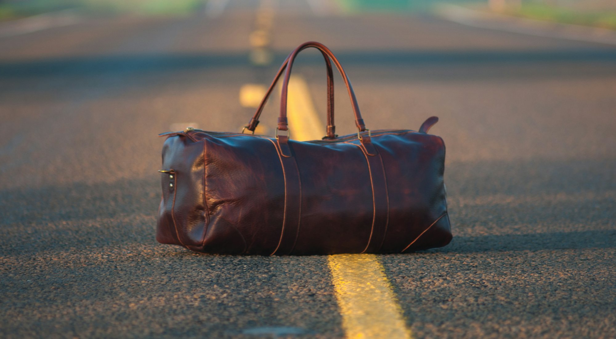 A leather duffel bag sitting in the middle of an empty road